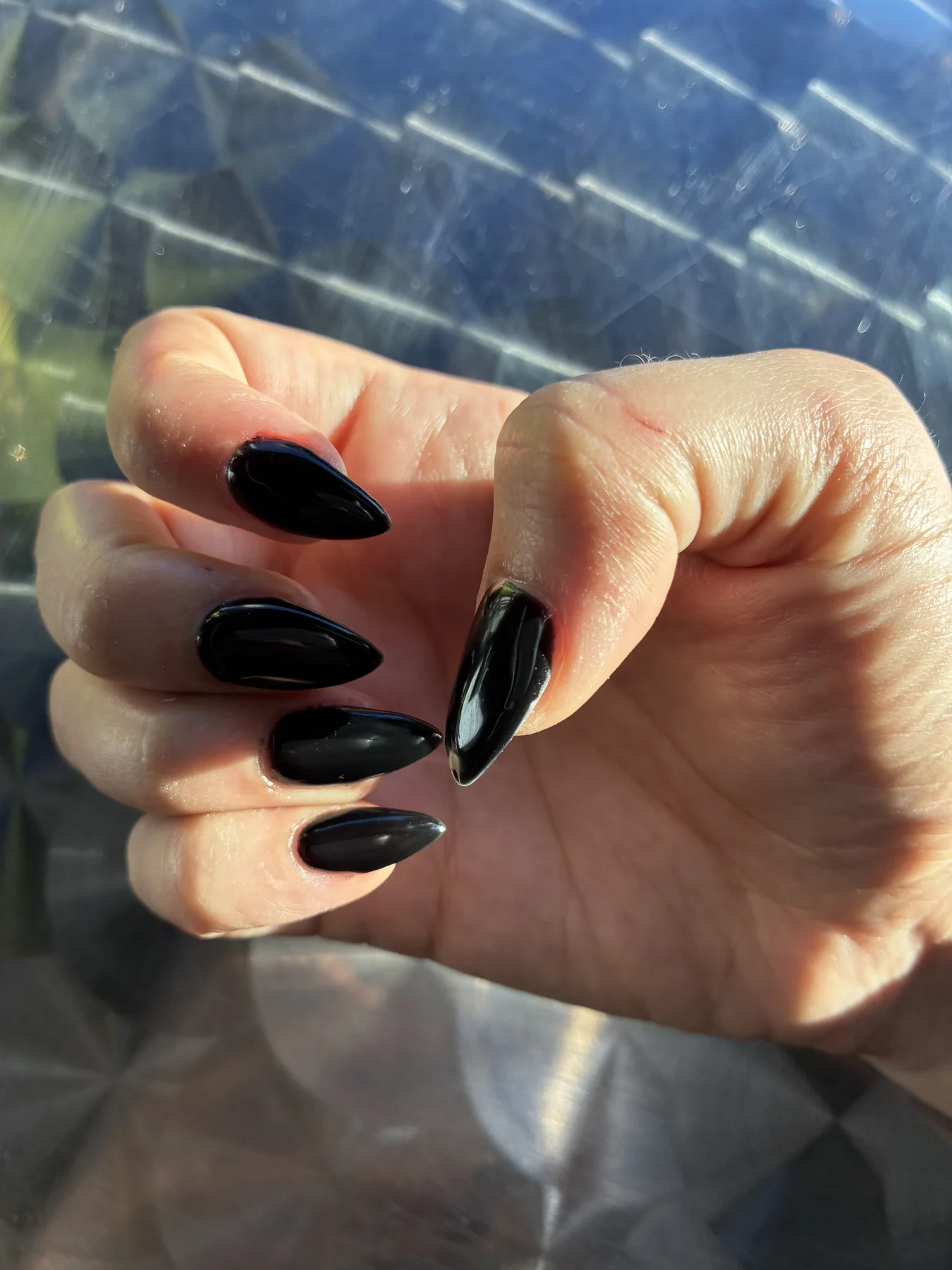 Long glossy black stiletto nails above metallic surface