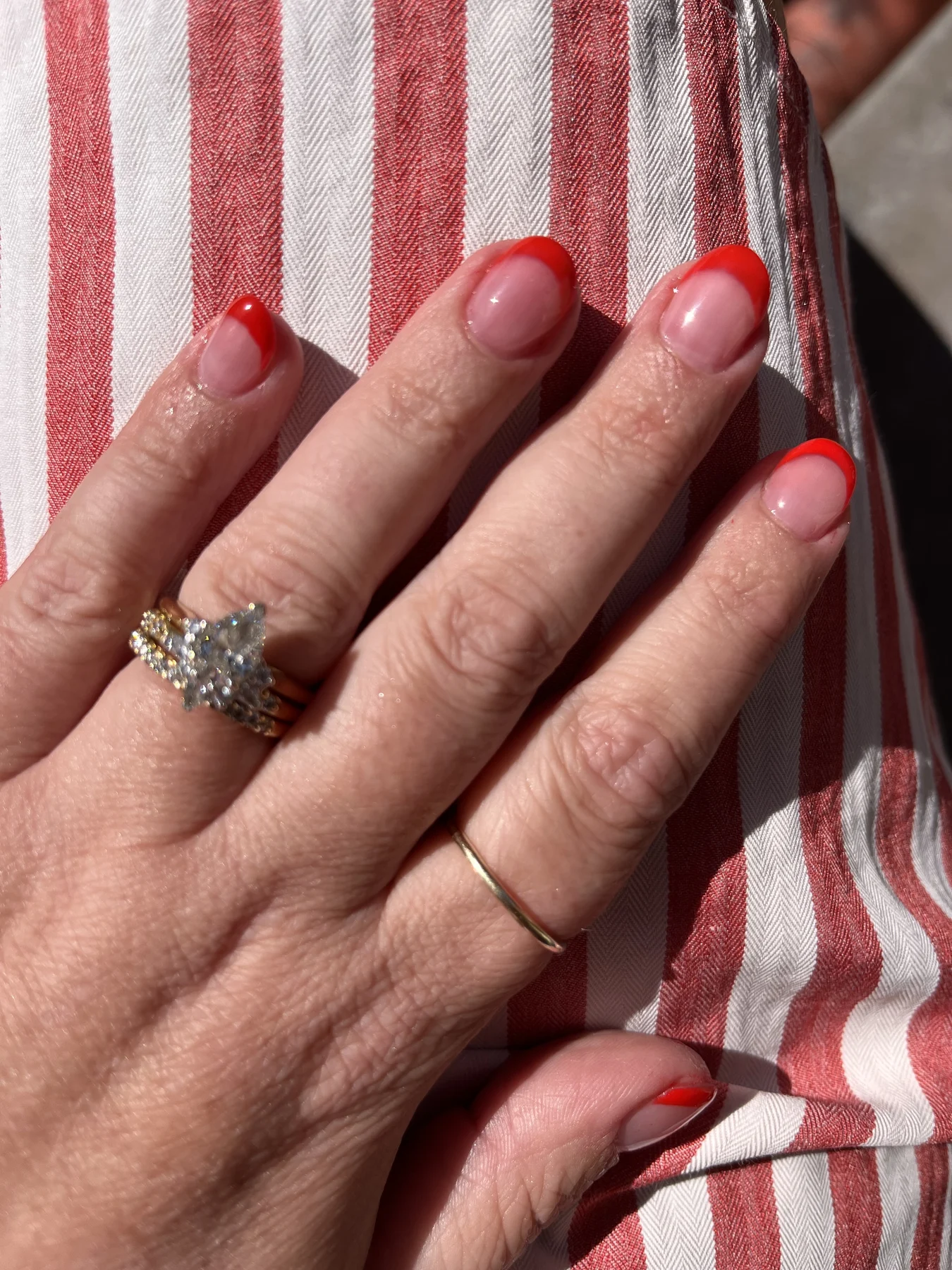 Red-tipped french nails with diamond ring on striped fabric
