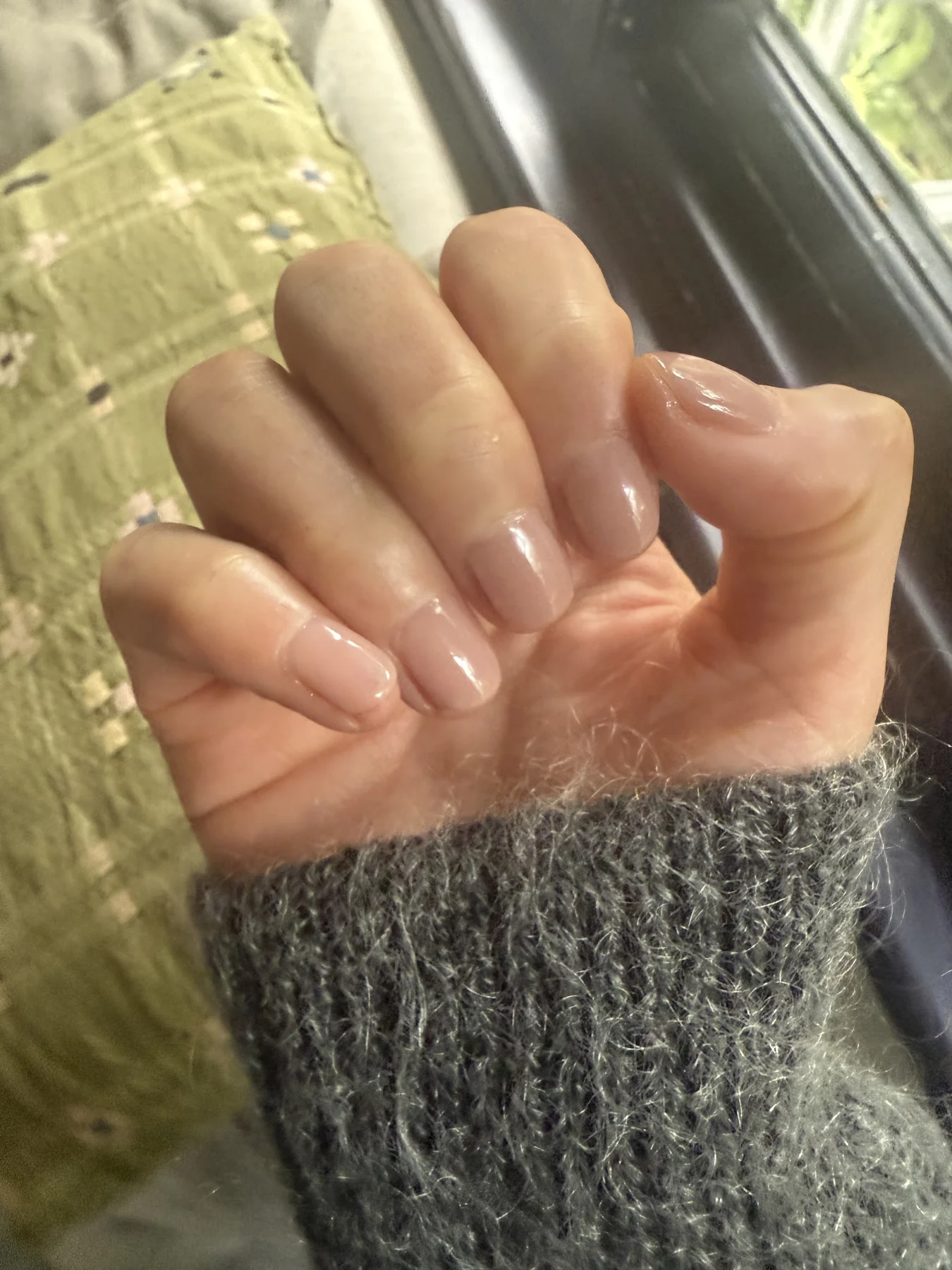 Long clear-nude nails against grey knit sleeve