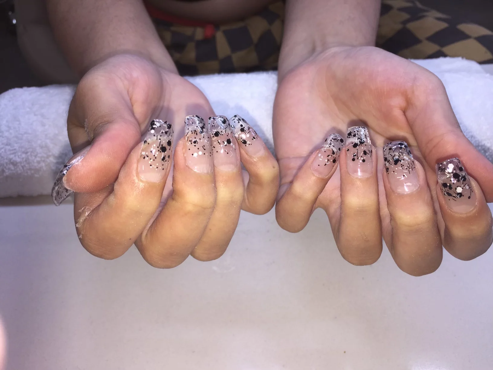 Black-speckled glitter ombre nails over white towel