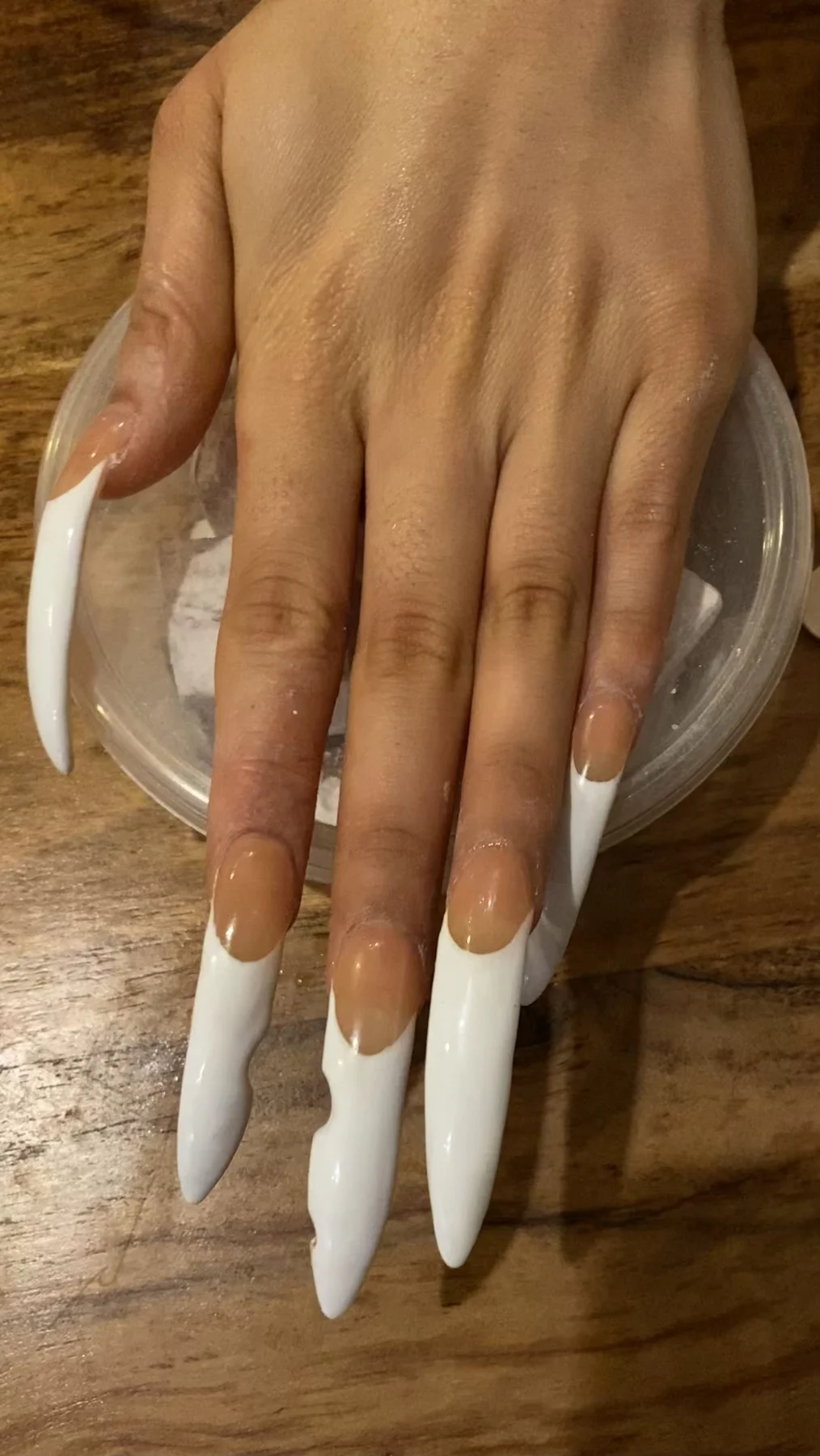 Very long white-tipped nude nails on wooden table