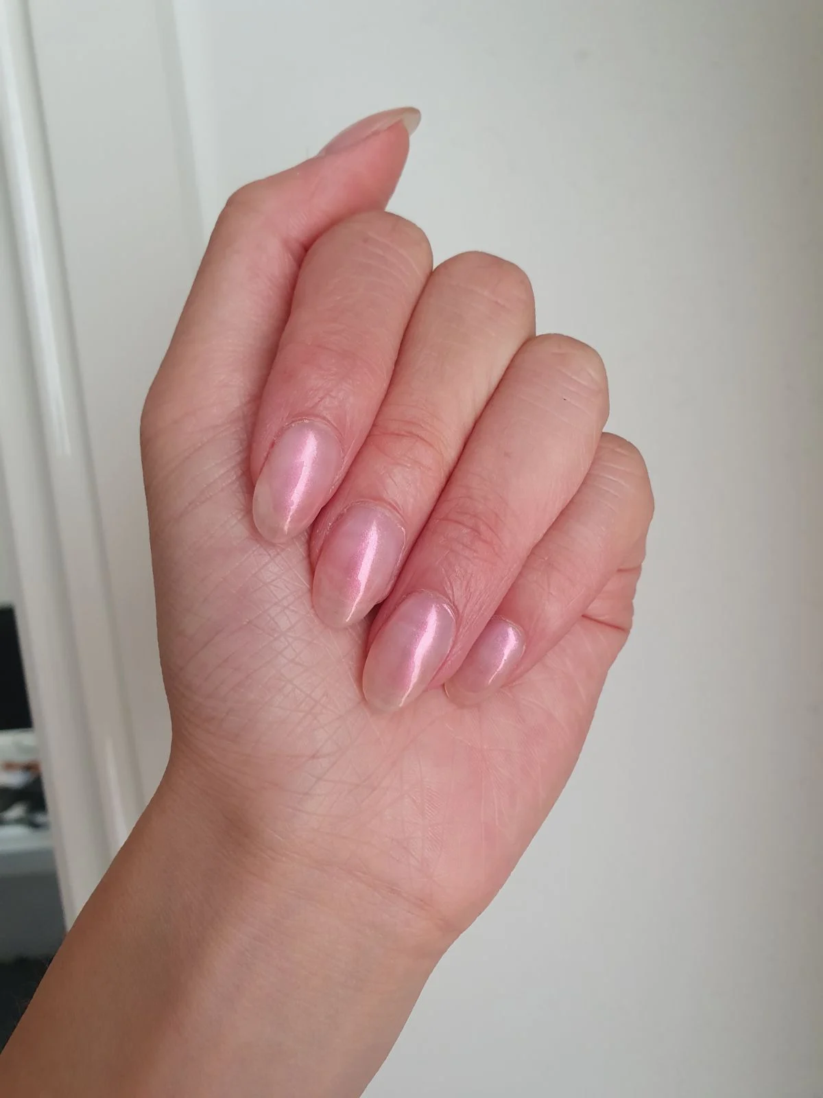 Glossy pale-pink almond nails against white wall