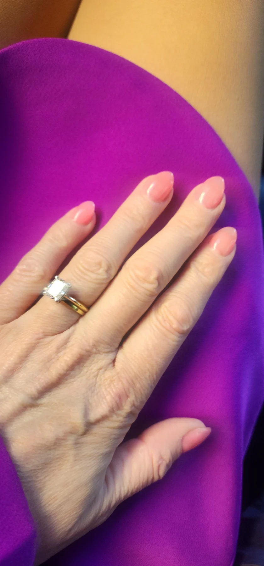 Soft-pink almond nails with solitaire ring on vivid purple fabric