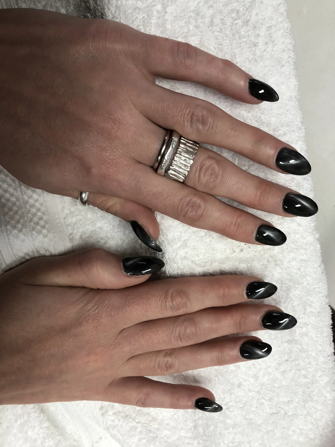 Glossy black almond nails with stacked silver rings