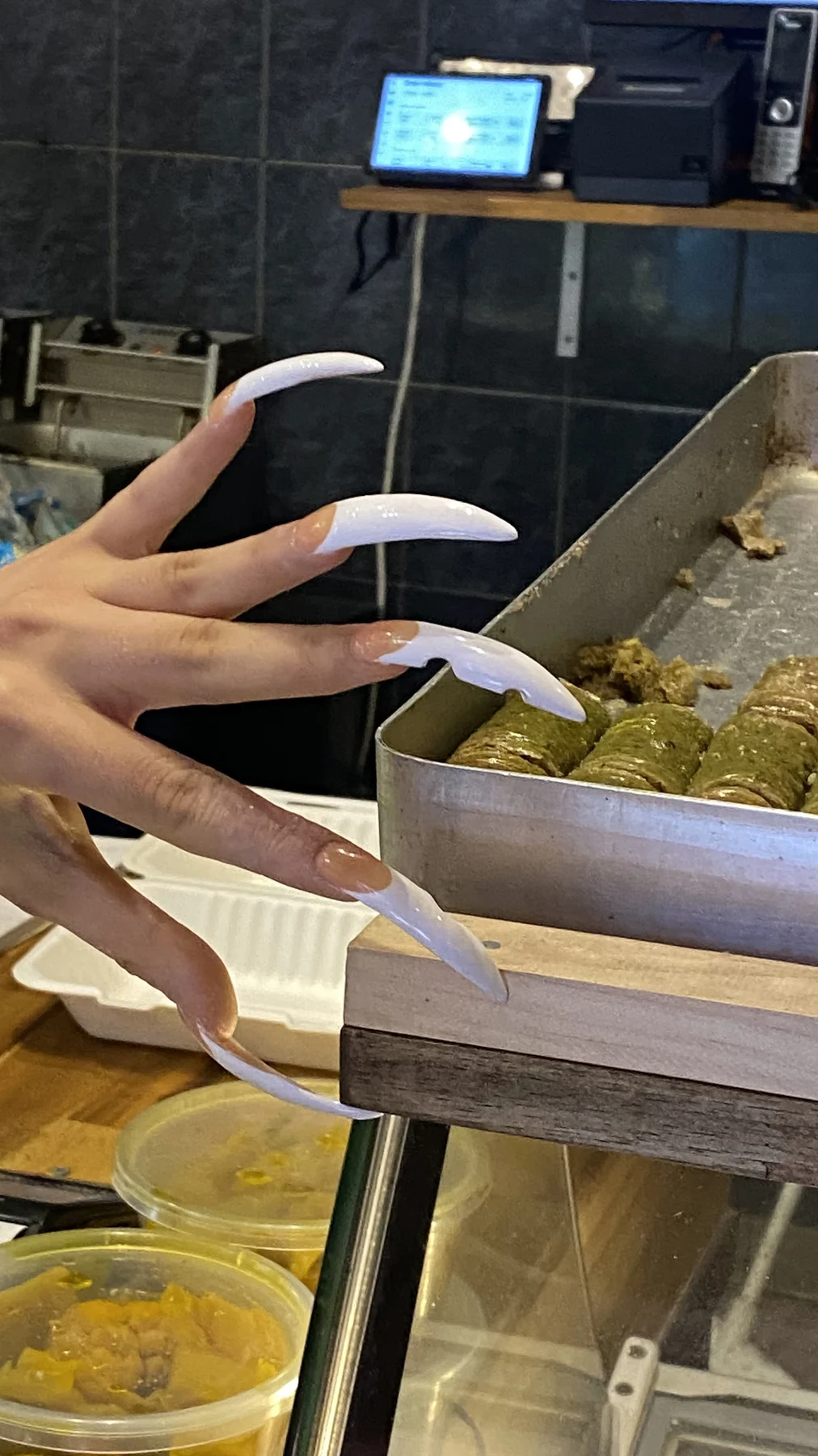 Long white-lilac nails reaching over a counter