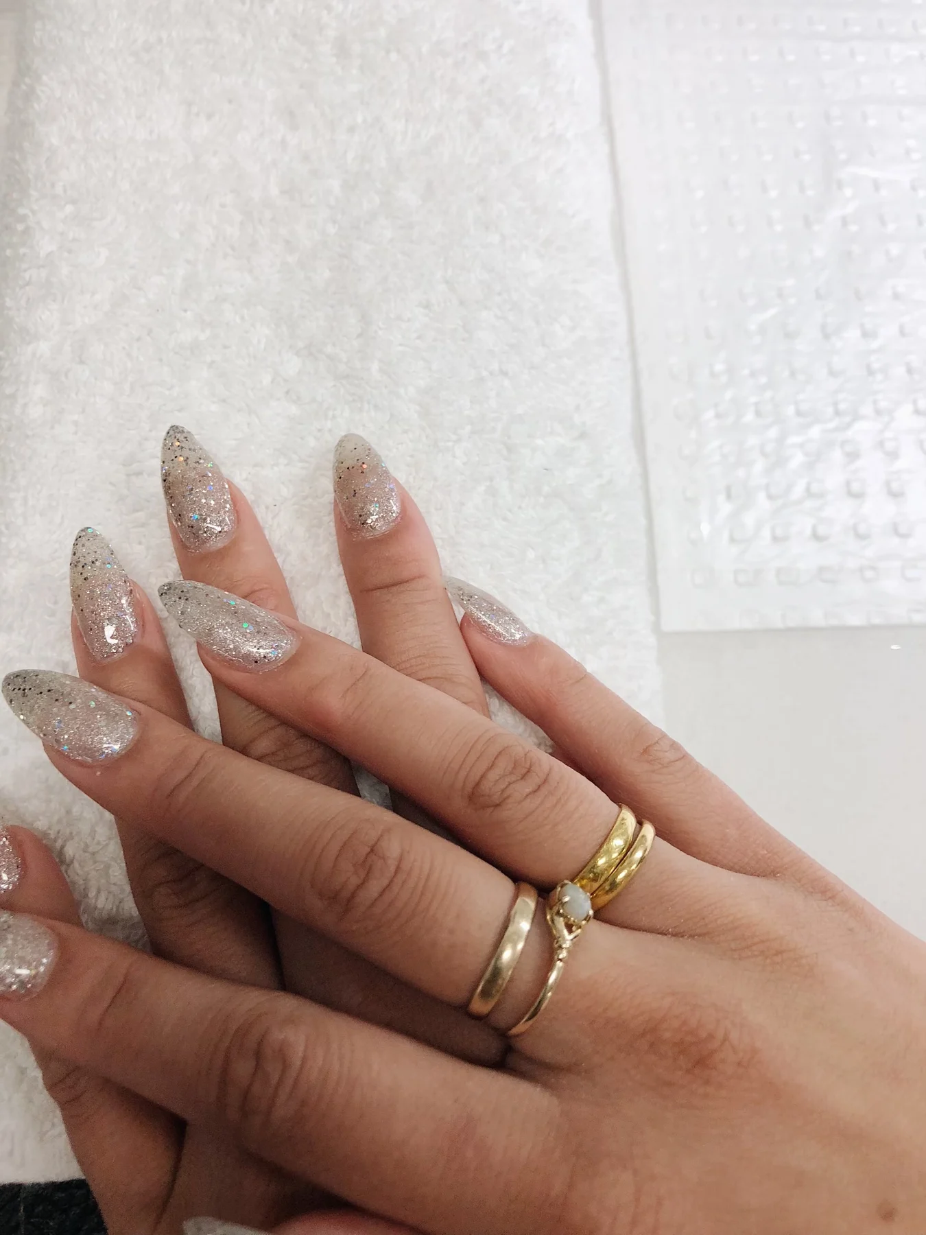 Silver-glitter nails with gold rings on white towel