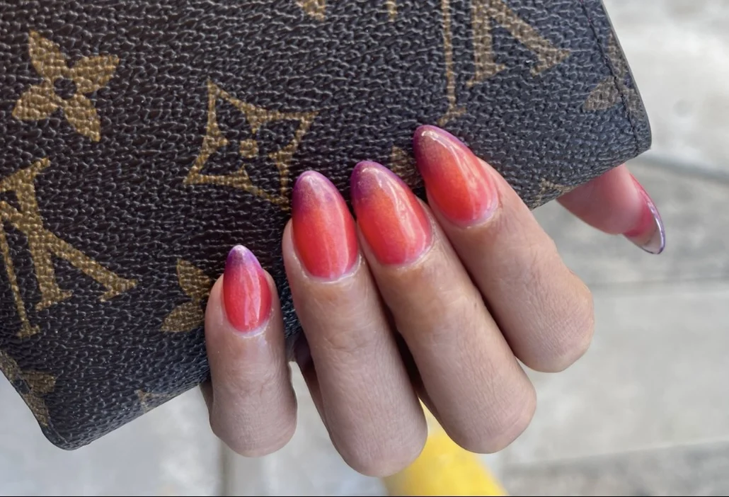 Pink-red ombre nails on monogrammed handbag